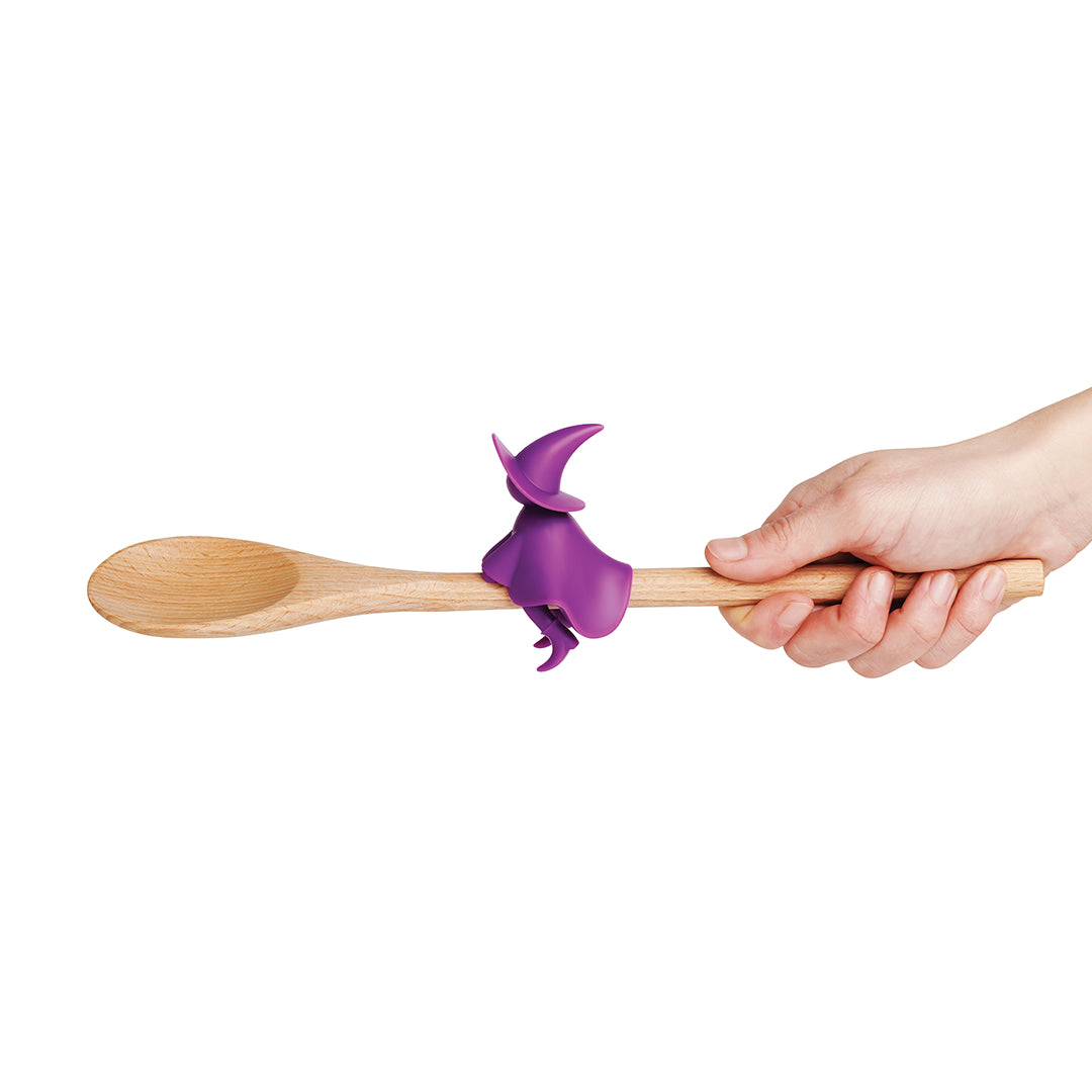 Hand with a wooden spoon featuring Agatha, a purple witch-shaped steam releaser.
