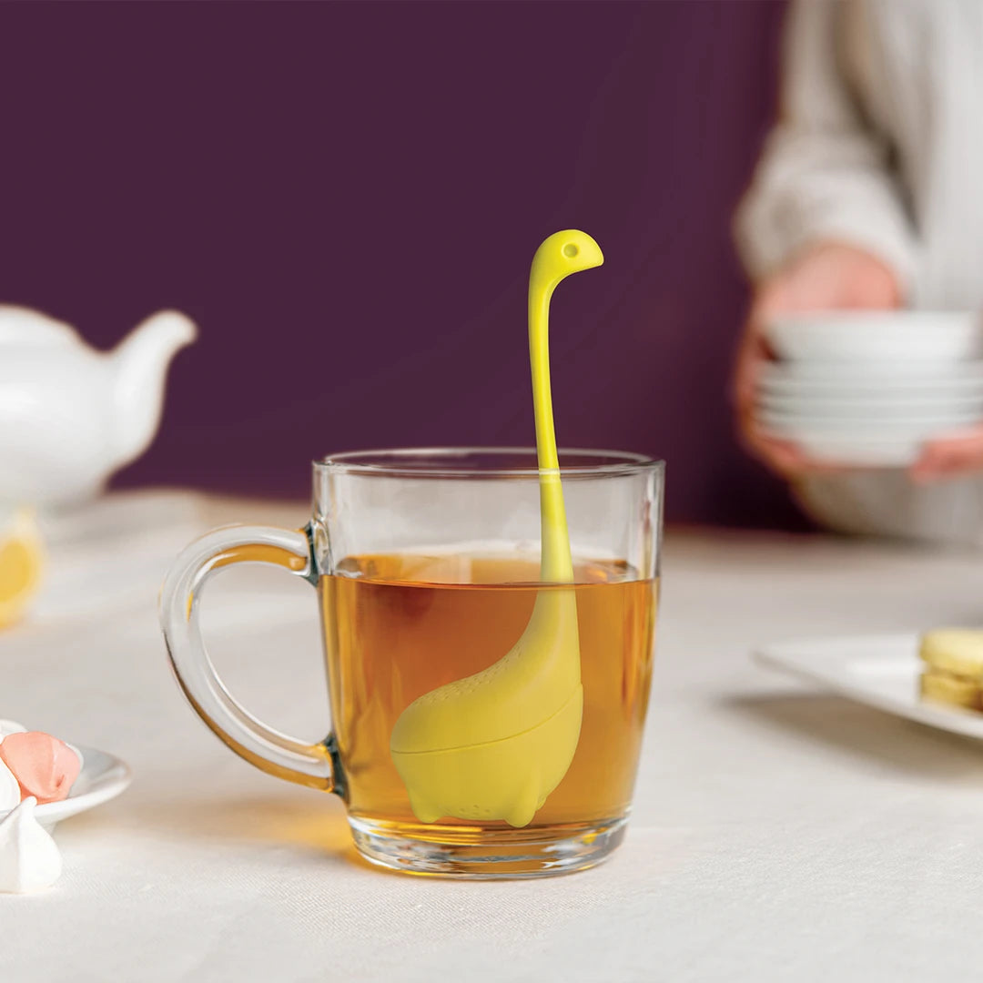 A Baby Nessie infuser from OTOTO Designs swims in a glass mug of tea on the table.