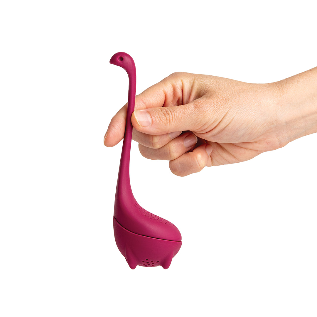 A hand holding a purple Baby Nessie tea infuser by OTOTO Designs.