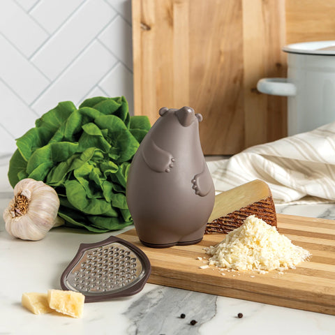 OTOTOs Barry bear grater next to lettuce, garlic, and mounds of grated cheese on a cutting board.
