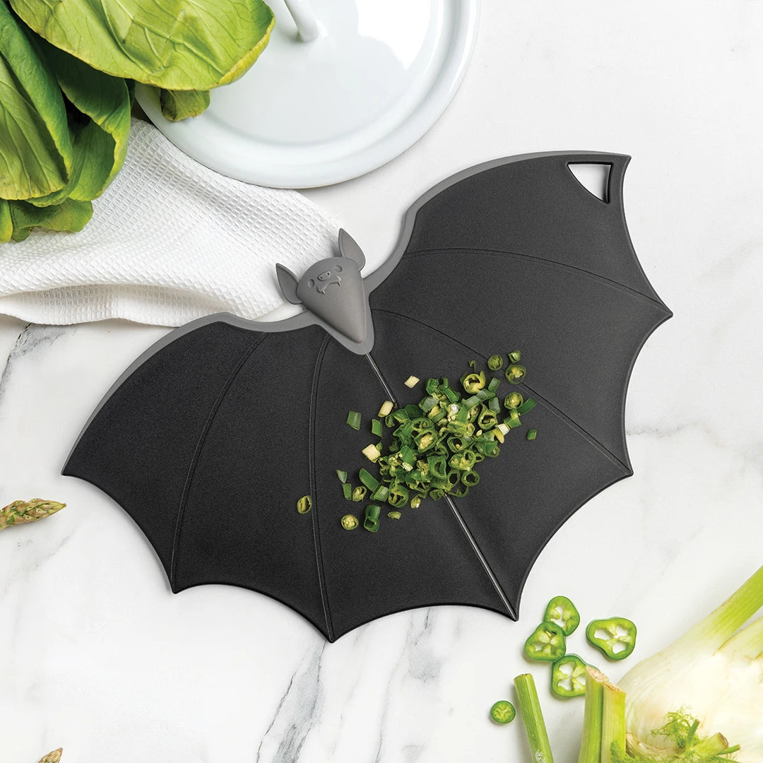 Batty cutting board with chopped green onions on marble, nestled by leafy greens.