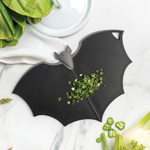 Batty cutting board with chopped green onions on marble, nestled by leafy greens.