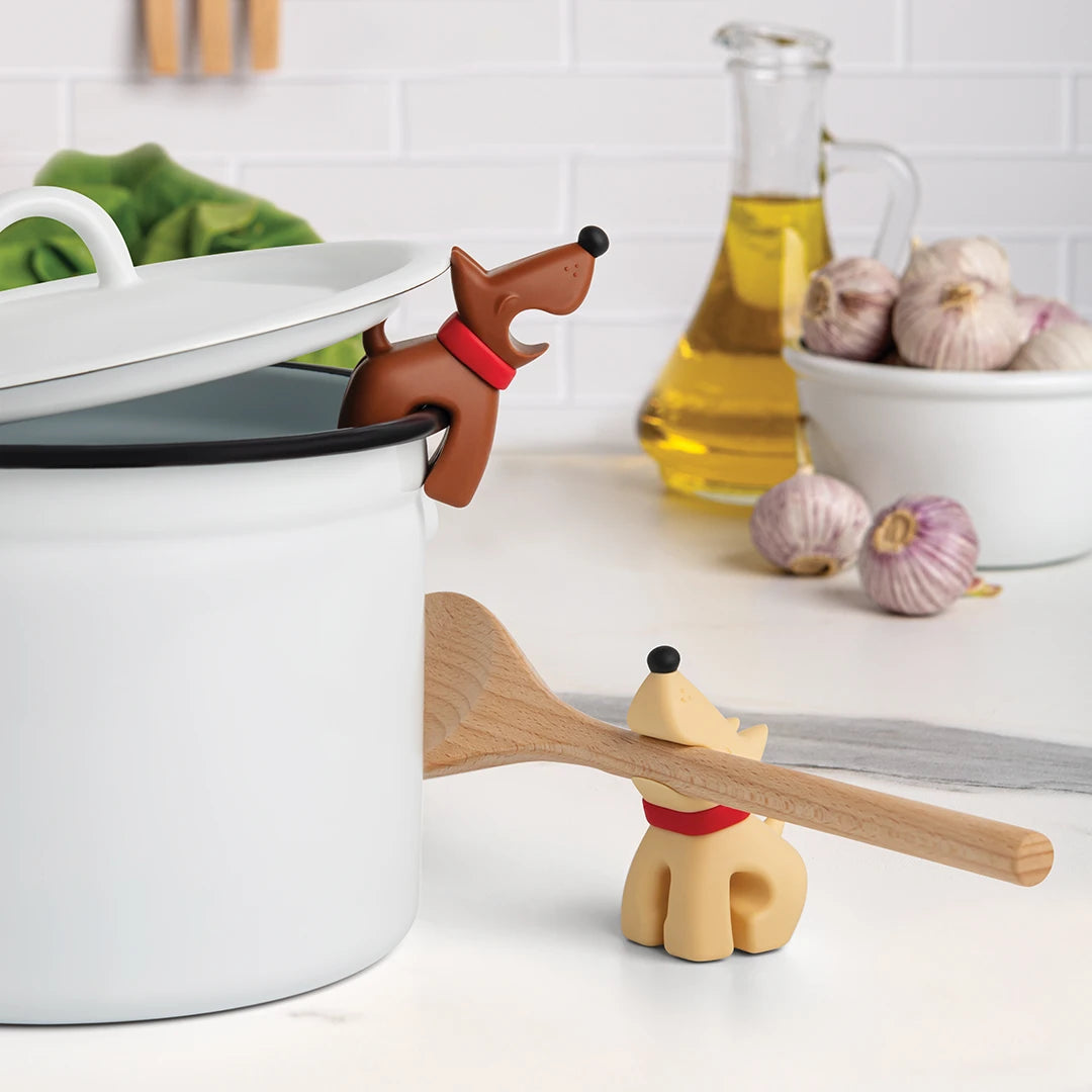 Buddy spoon holder and steam releaser on a kitchen counter with garlic and oil in the background.