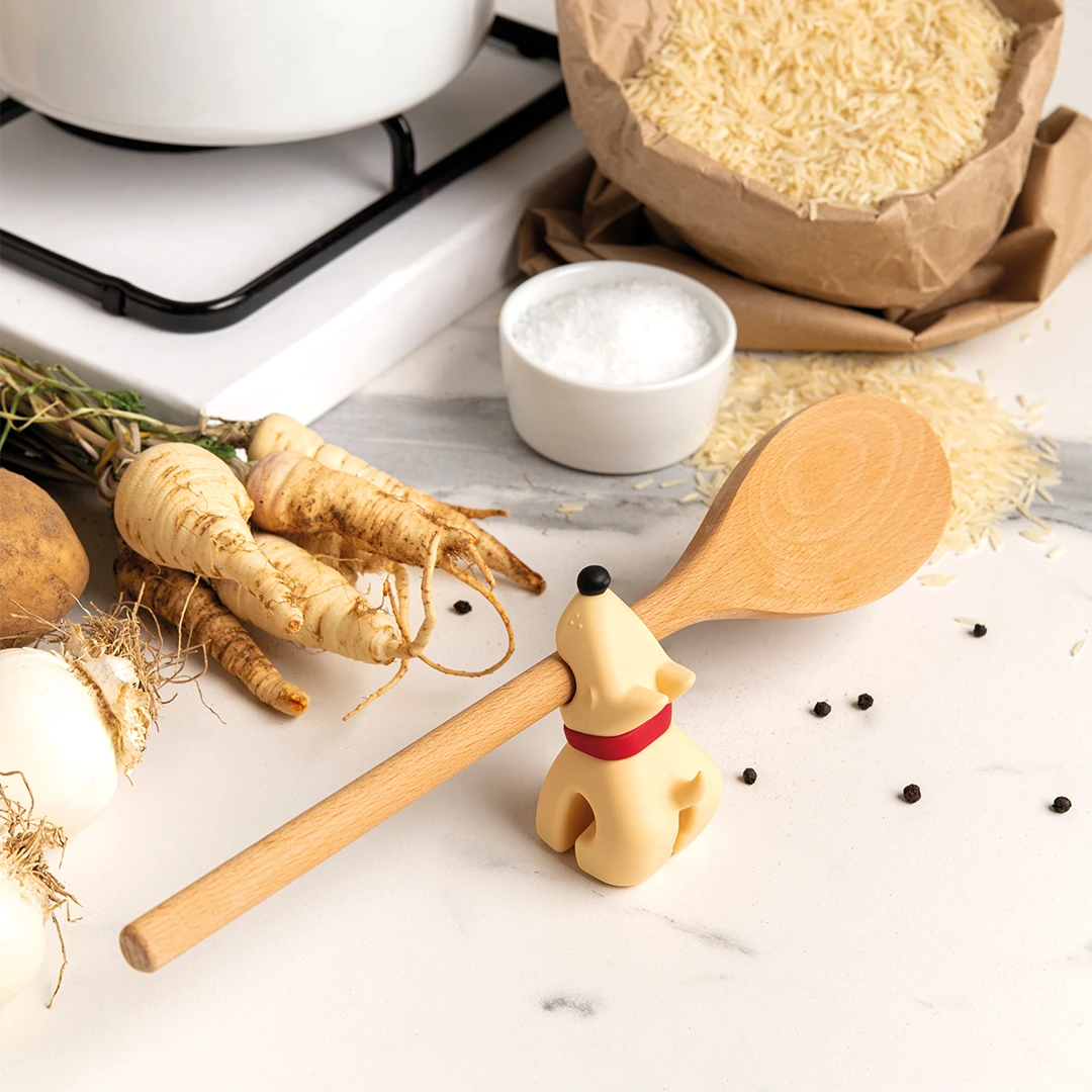 Buddy spoon with dog handle on counter, surrounded by parsnips, rice, and peppercorns in a cozy kitchen.