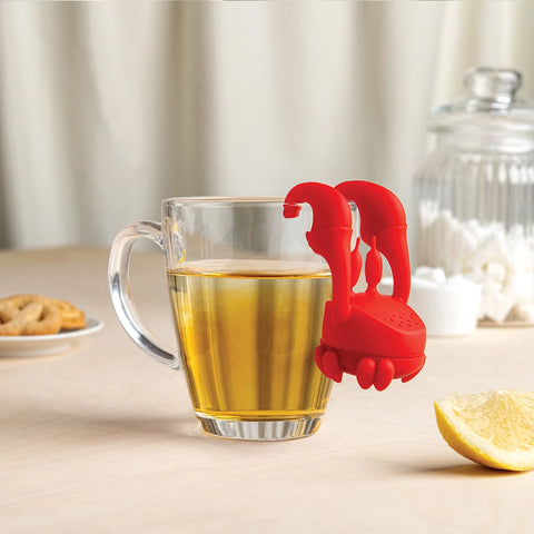 Crab Tea infuser on a cup of tea, with cookies, a lemon slice, and sugar nearby.