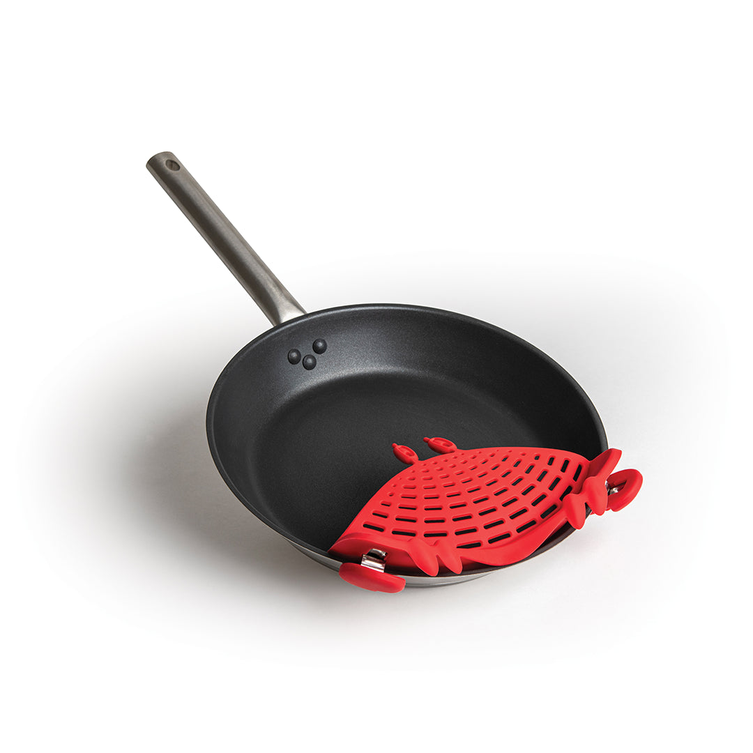A black frying pan with a Crabby red silicone strainer clipped to its side handle.