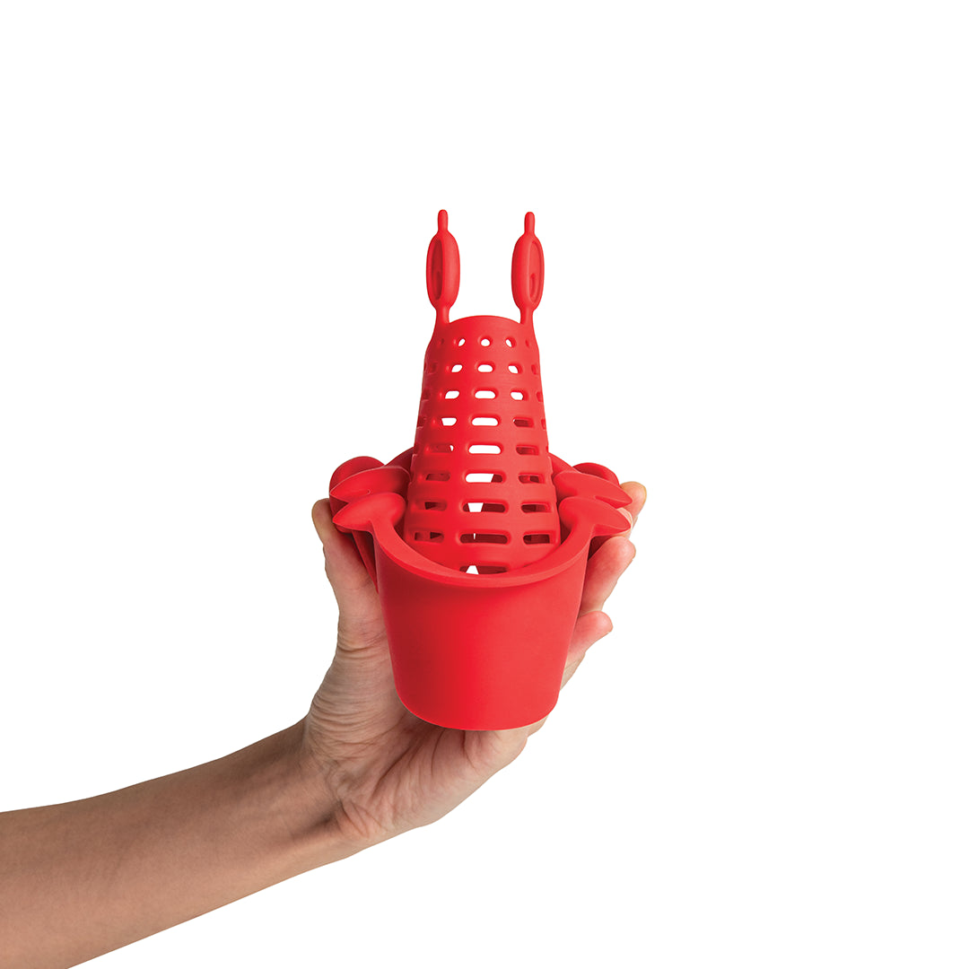 Hand holding OTOTOs Crabby, a red silicone lobster-shaped tea infuser and quirky kitchen accessory.
