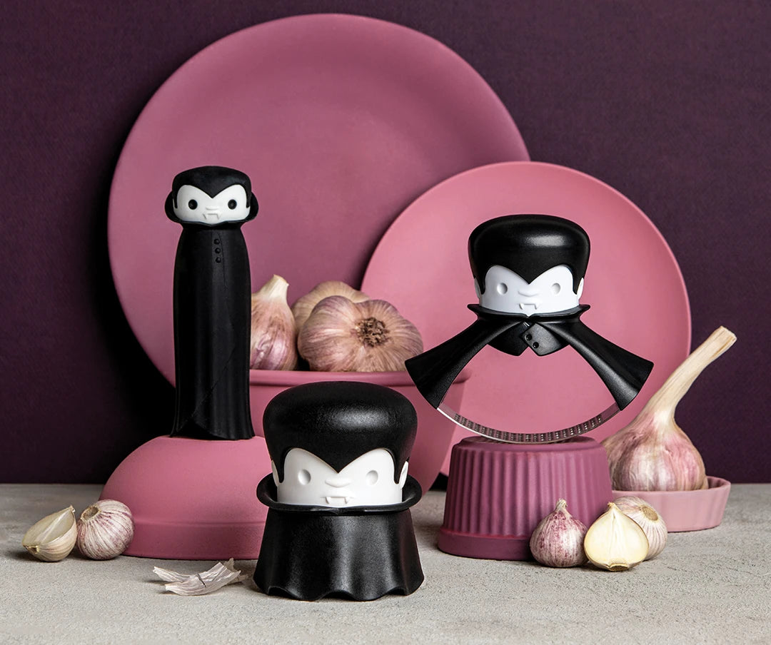 Three vampire-themed kitchen tools with pink plates and garlic bulbs against a dark background.