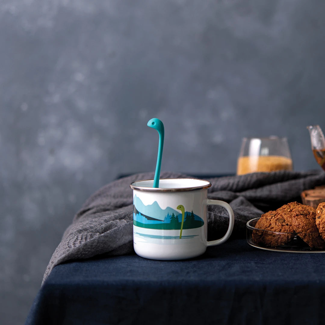 Cup of Nessie ladle in a mountain mug with cookies on a dark table.