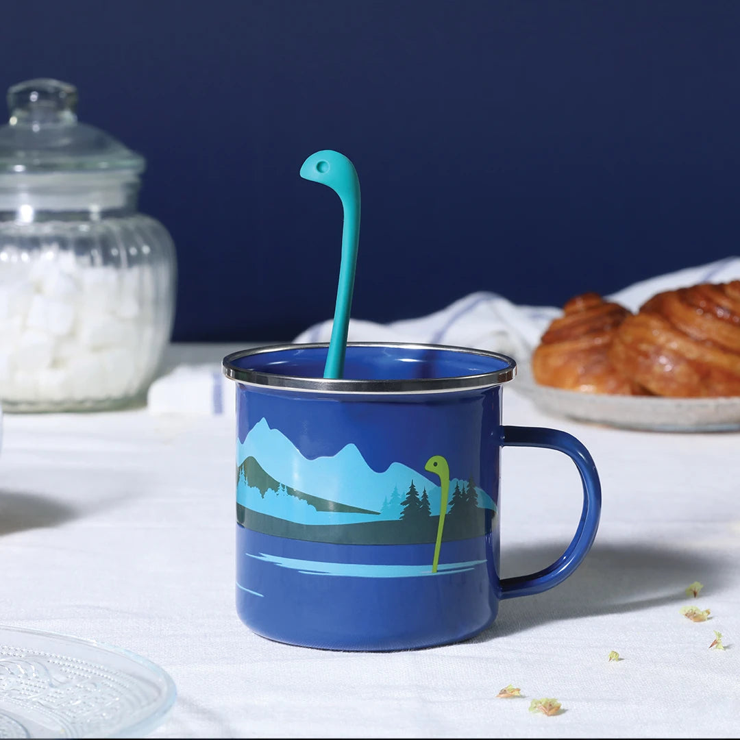 Cup of Nessie with OTOTO tea infuser, a blue mug with mountains, croissants, and jar on the table.