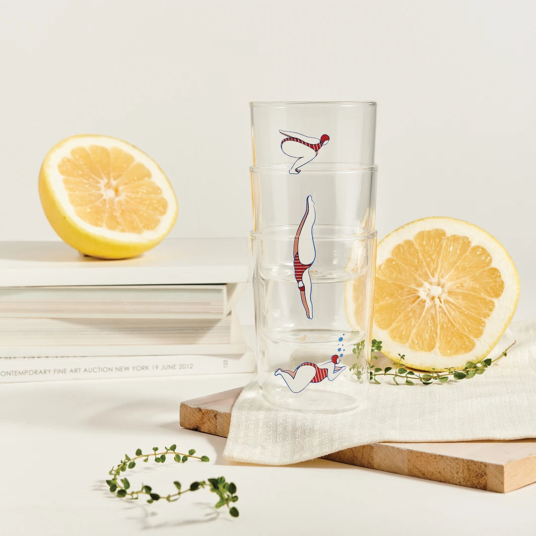 Deep Dive glasses by OTOTO with diving illustrations, lemon halves, and green sprigs on a cloth napkin.