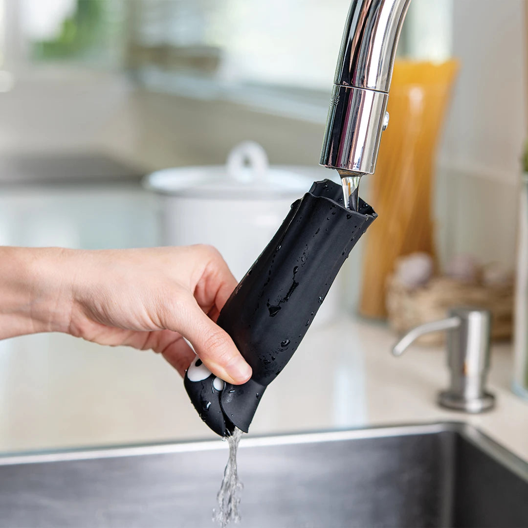 A person rinses a Drac N Roll garlic peeler under a kitchen faucet.