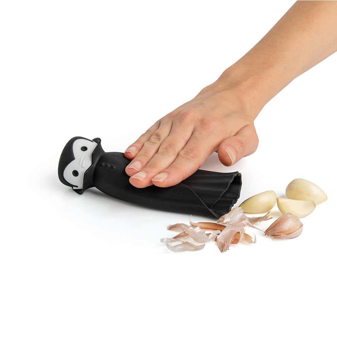 Hand using the Drac N Roll peeler to remove garlic skins on a white surface.