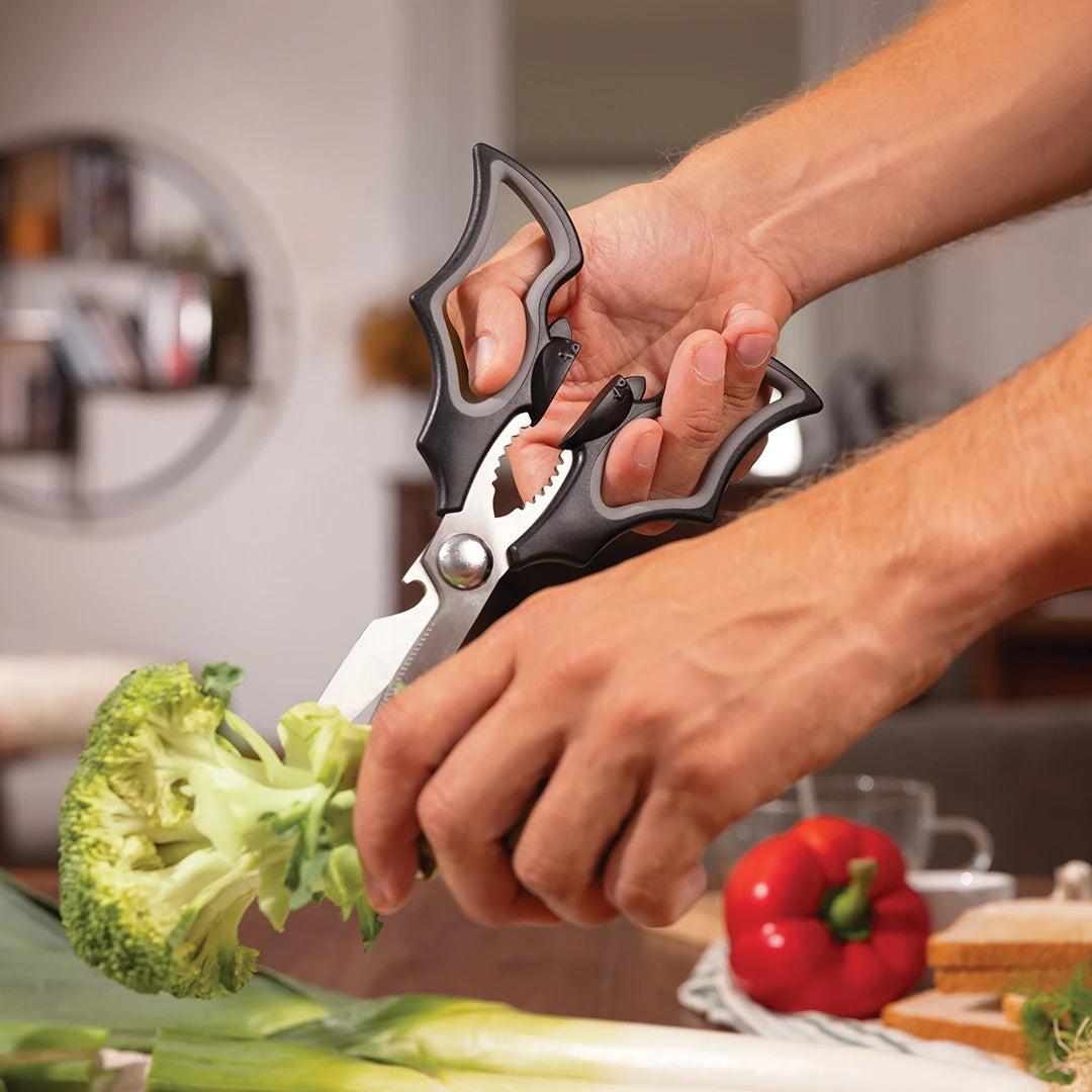 Hands using Elizabat scissors to cut broccoli in a home setting.