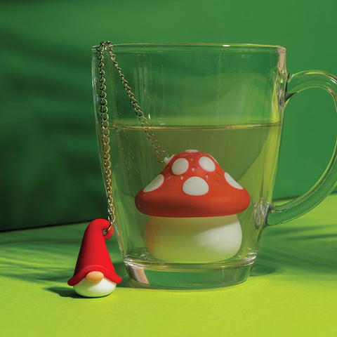 Enchan-Tea by OTOTO: A whimsical mushroom tea infuser in a glass cup with gnome charm on a green backdrop.
