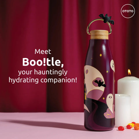 A Boo!tle purple OTOTO insulated water bottle with ghost and bat designs sits by a lit candle and candy.