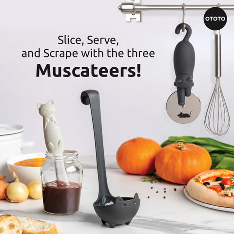Three Muscateers cat-themed utensils—a soup ladle, pizza cutter, and jar scraper—in a modern kitchen.