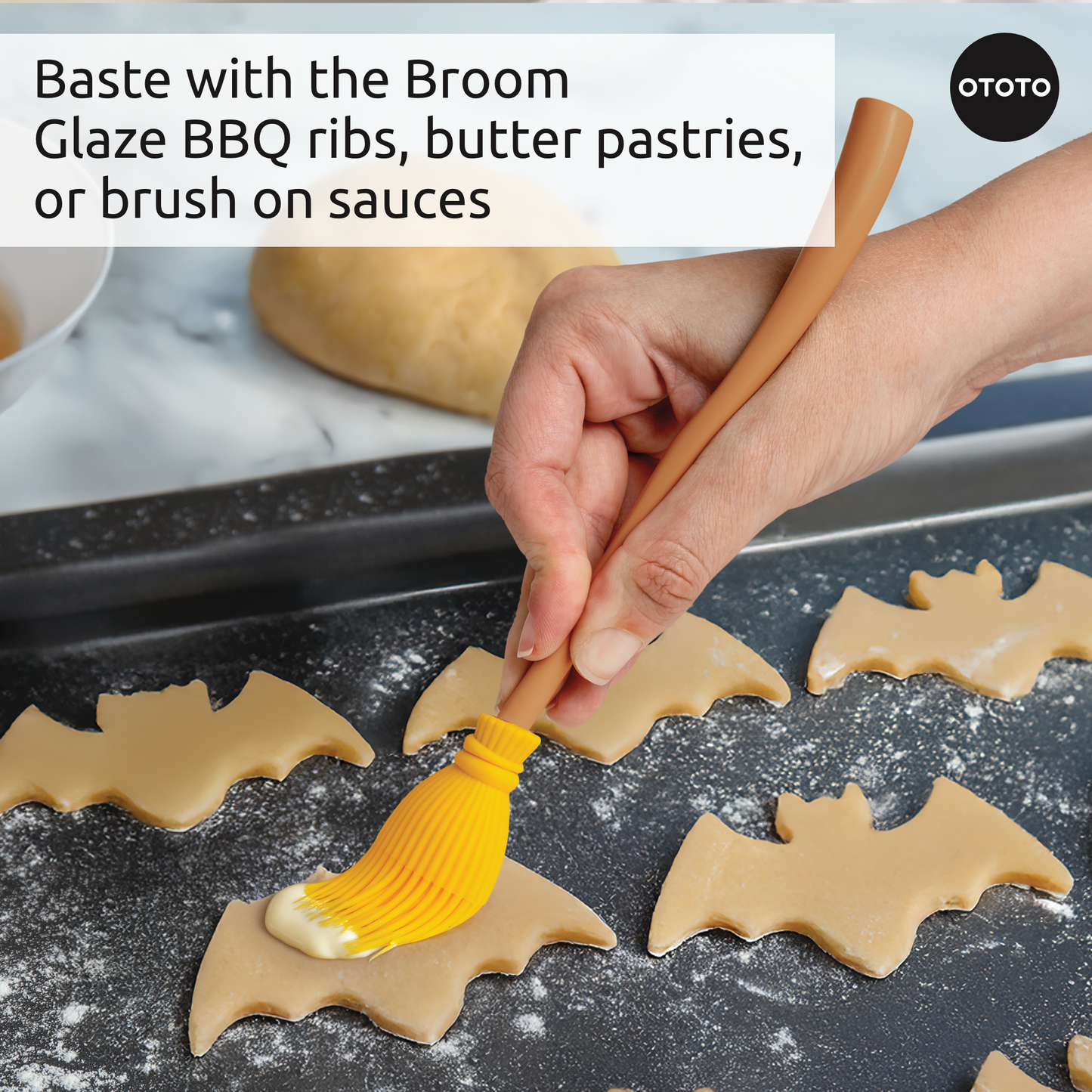 A hand uses the Witchin yellow basting brush to glaze bat-shaped cookie dough on a baking tray.