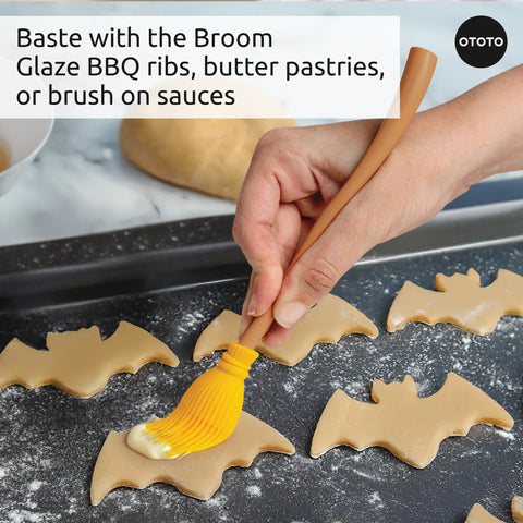 Hand using the Witchin heat resistant basting brush to baste bat-shaped cookies on a baking tray.