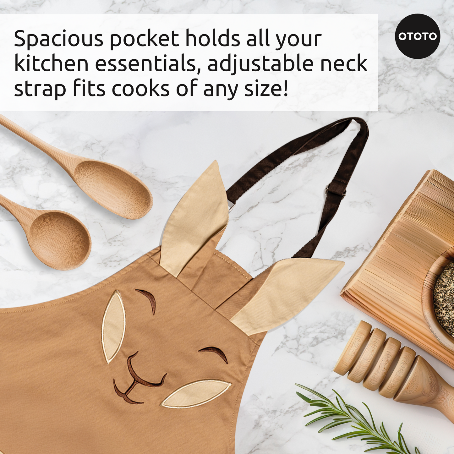 Aproo bunny face kitchen apron with ears, wooden utensils, and oven mitts on a white countertop.