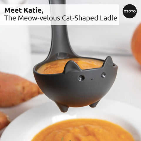 A Muscateers cat soup ladle filled with soup is held above a white bowl with orange vegetables.