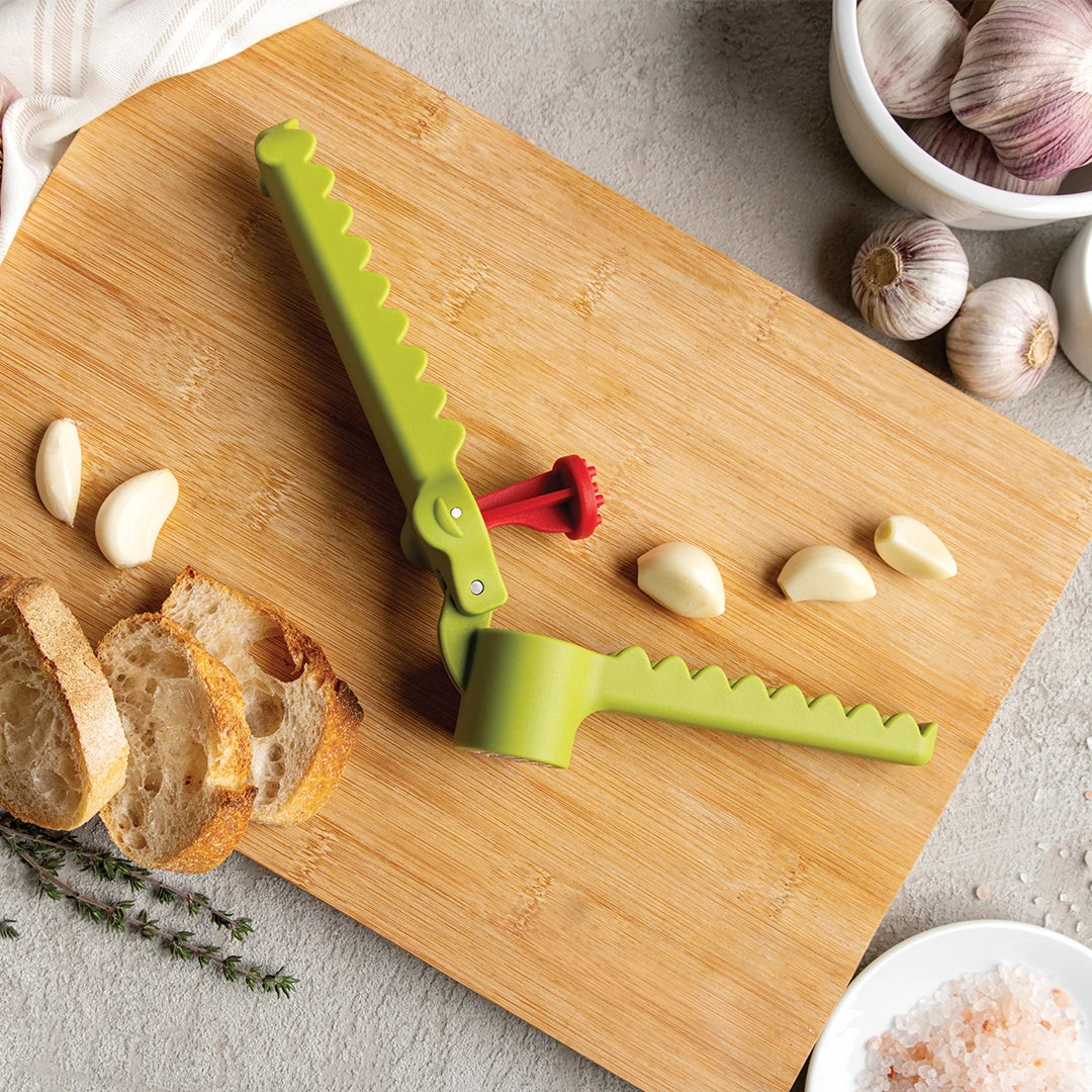 The Garligator presses garlic on a wooden board with cloves, bread slices, and salt.