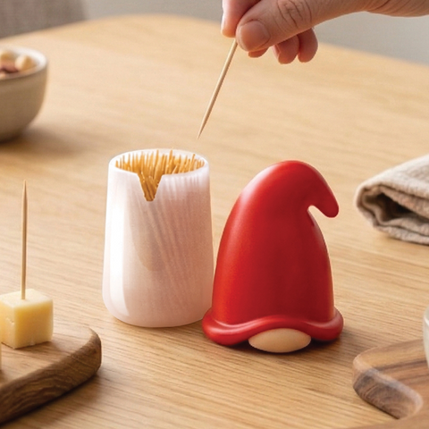 Hand taking a toothpick from the Gnomeo dispenser by OTOTO on a wooden table.