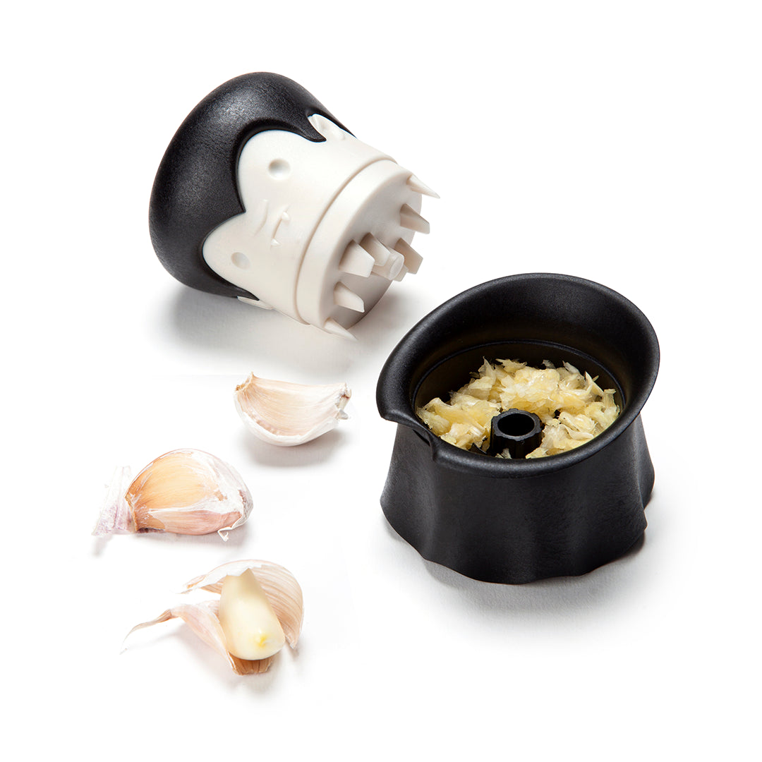 Gracula garlic crusher, featuring a black and white bat design, sits beside peeled and crushed cloves.