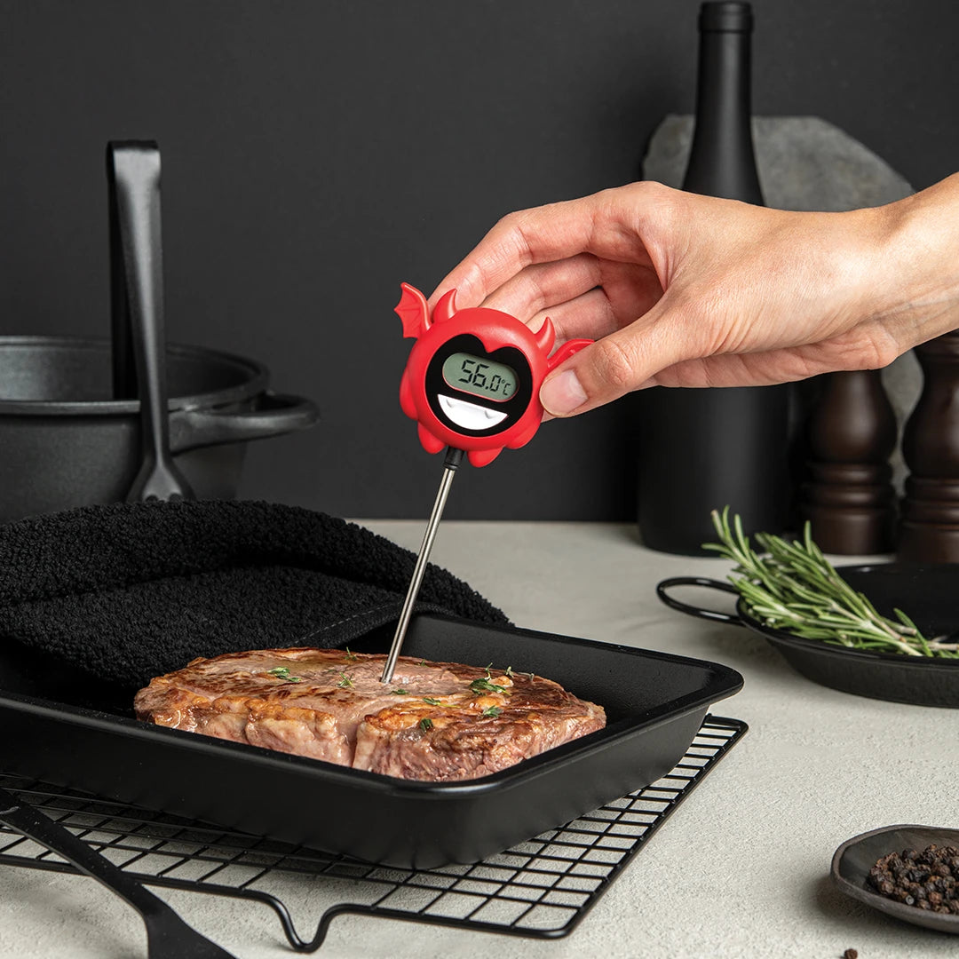 Hand using an OTOTO Hell Done meat thermometer to check a steaks temperature in a black baking dish.
