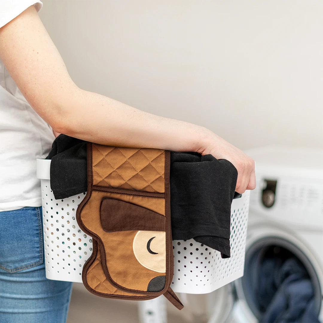 Person holding a laundry basket with OTOTOs Hot-dog Mitts and black clothes near a washing machine.