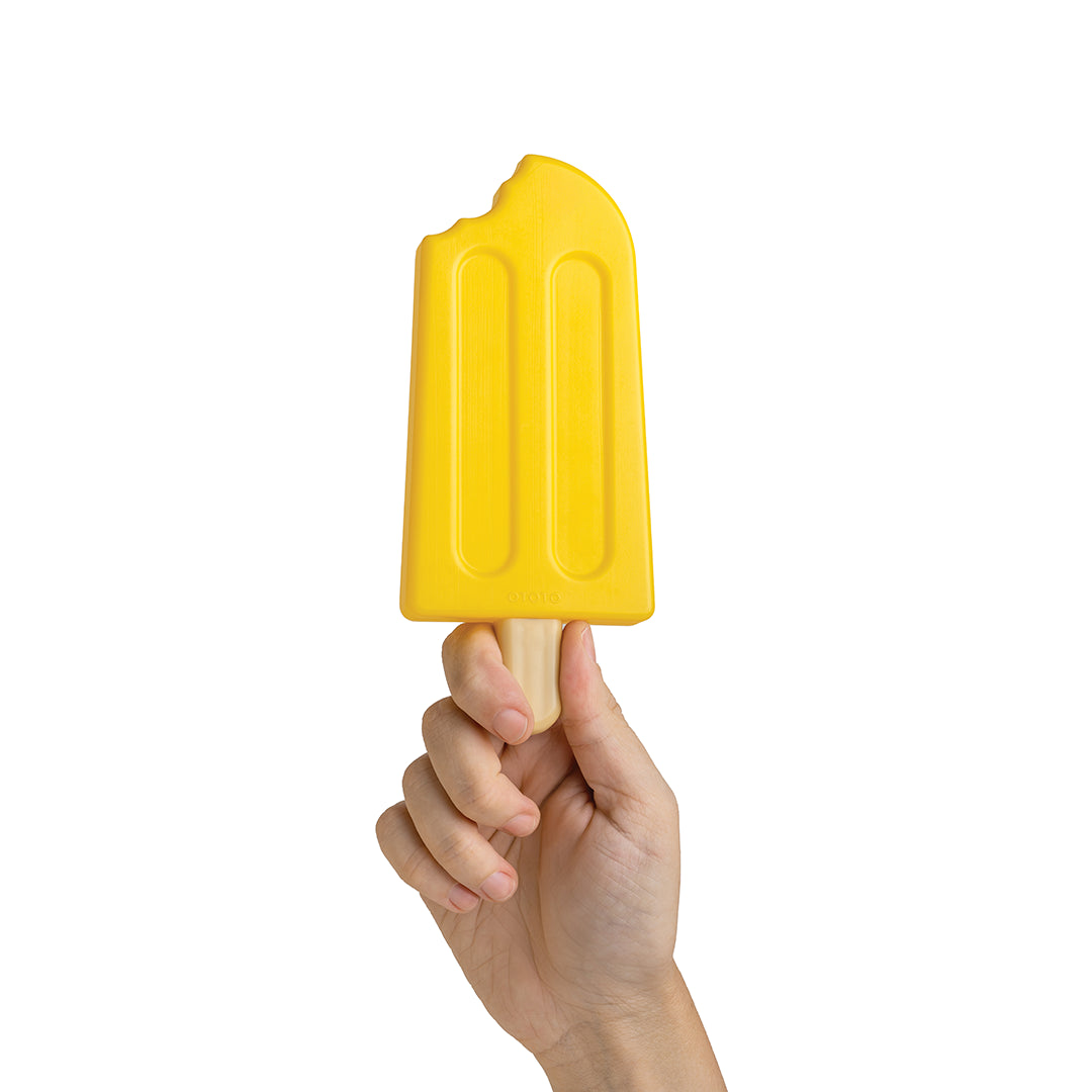 A hand holds OTOTO’s Ice Pop Ice Pack, yellow with a bite design, against a white background.