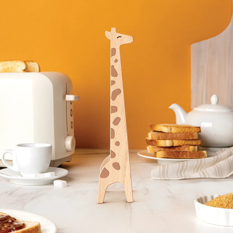 The giraffe-shaped wooden Jerry tongs by OTOTO stand on a kitchen counter next to a teapot and toast.