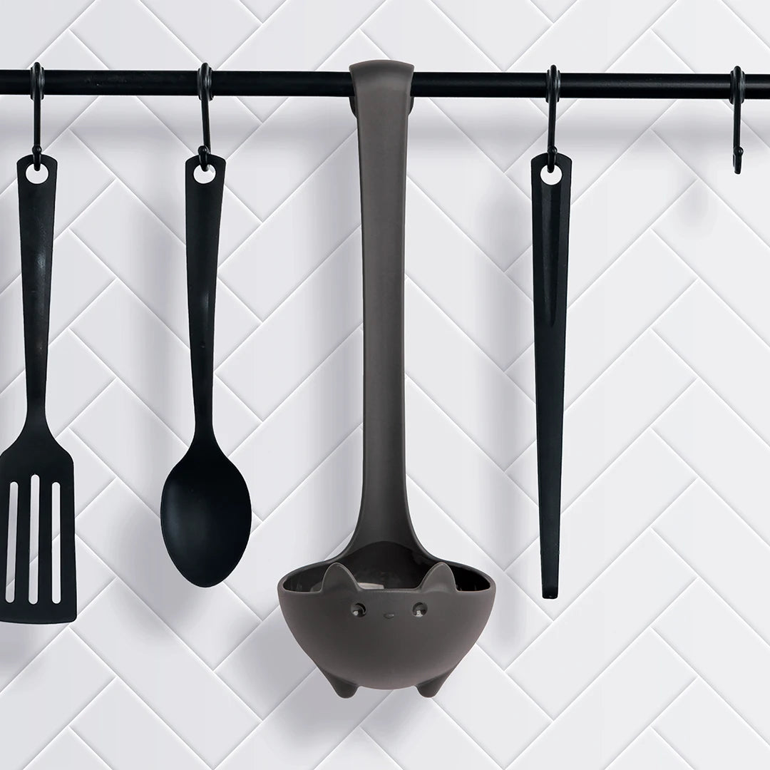 OTOTOs Katie soup ladle, spatula, spoon, and tongs hang on hooks against a white tiled wall.