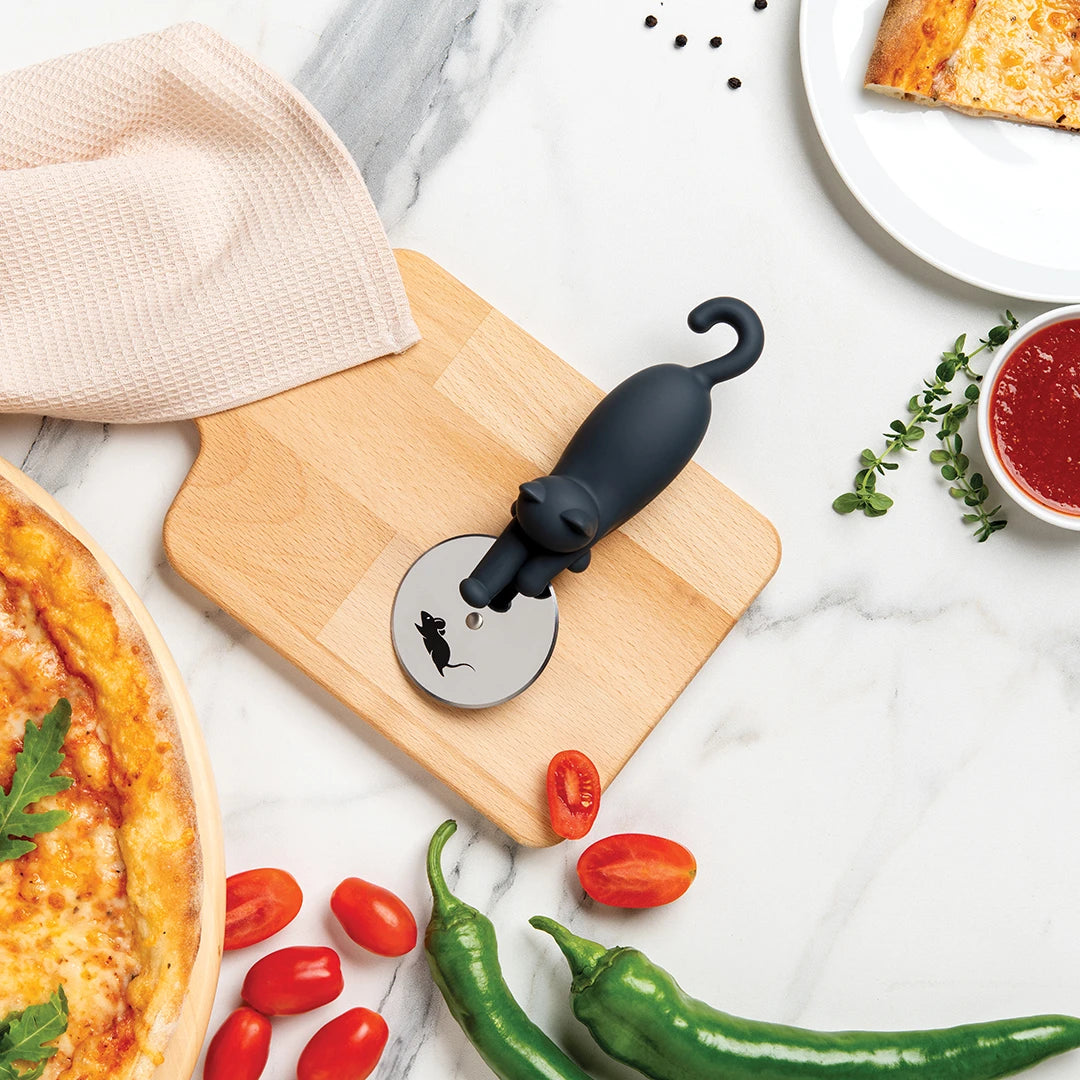 Kitty-Cut pizza cutter with a cat-shaped handle on a wooden board surrounded by fresh ingredients.