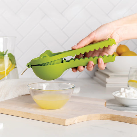 Hand using the Lemongator citrus juicer, BPA-free and ergonomic, shaped like a green alligator in the kitchen.