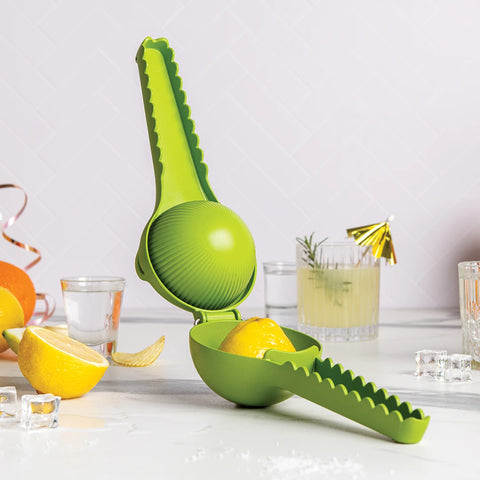 Lemongator juicer with lemon halves on a white surface, next to glasses and ice cubes.