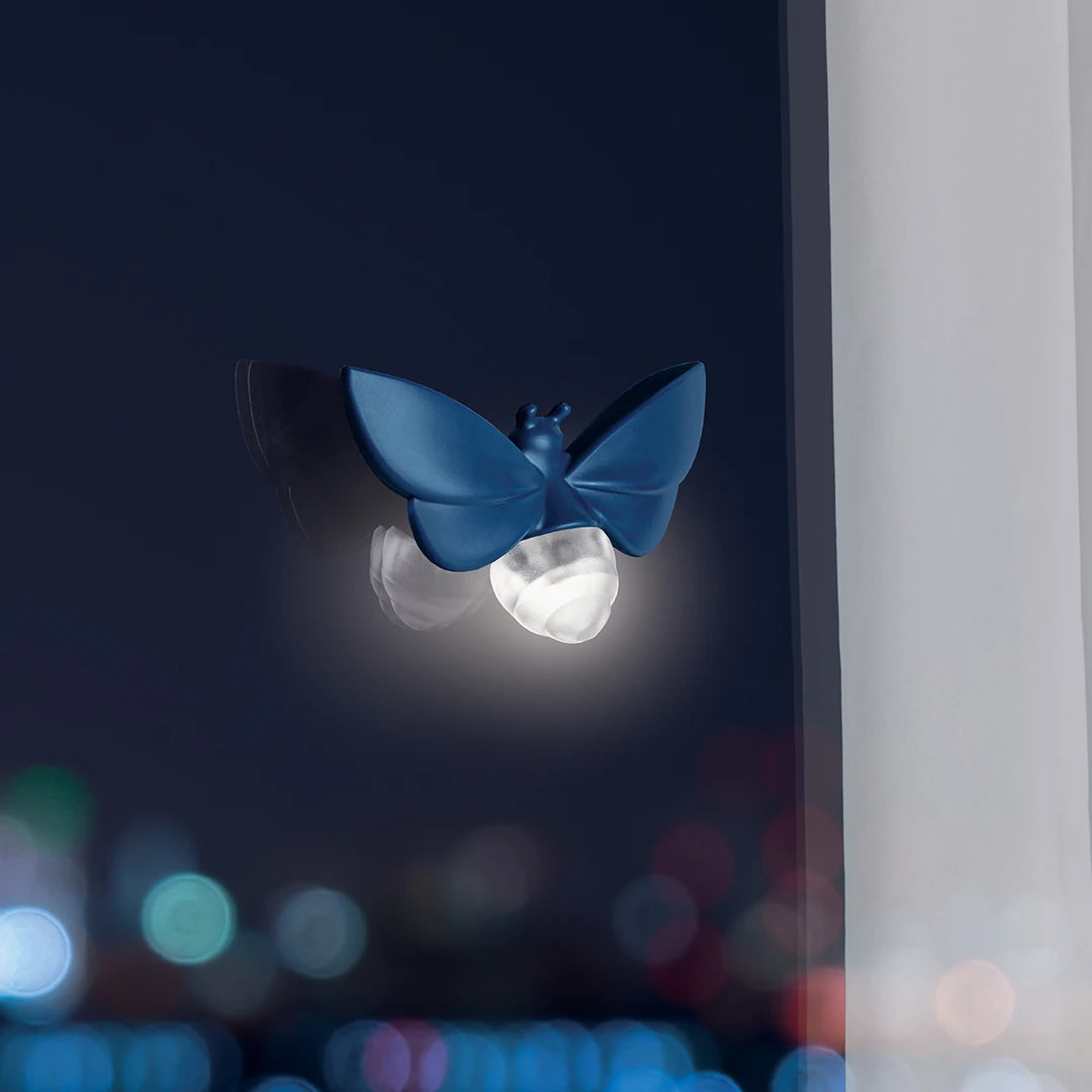 The OTOTO Lightbug beams in blue on the window, glowing softly against blurred city lights beyond.
