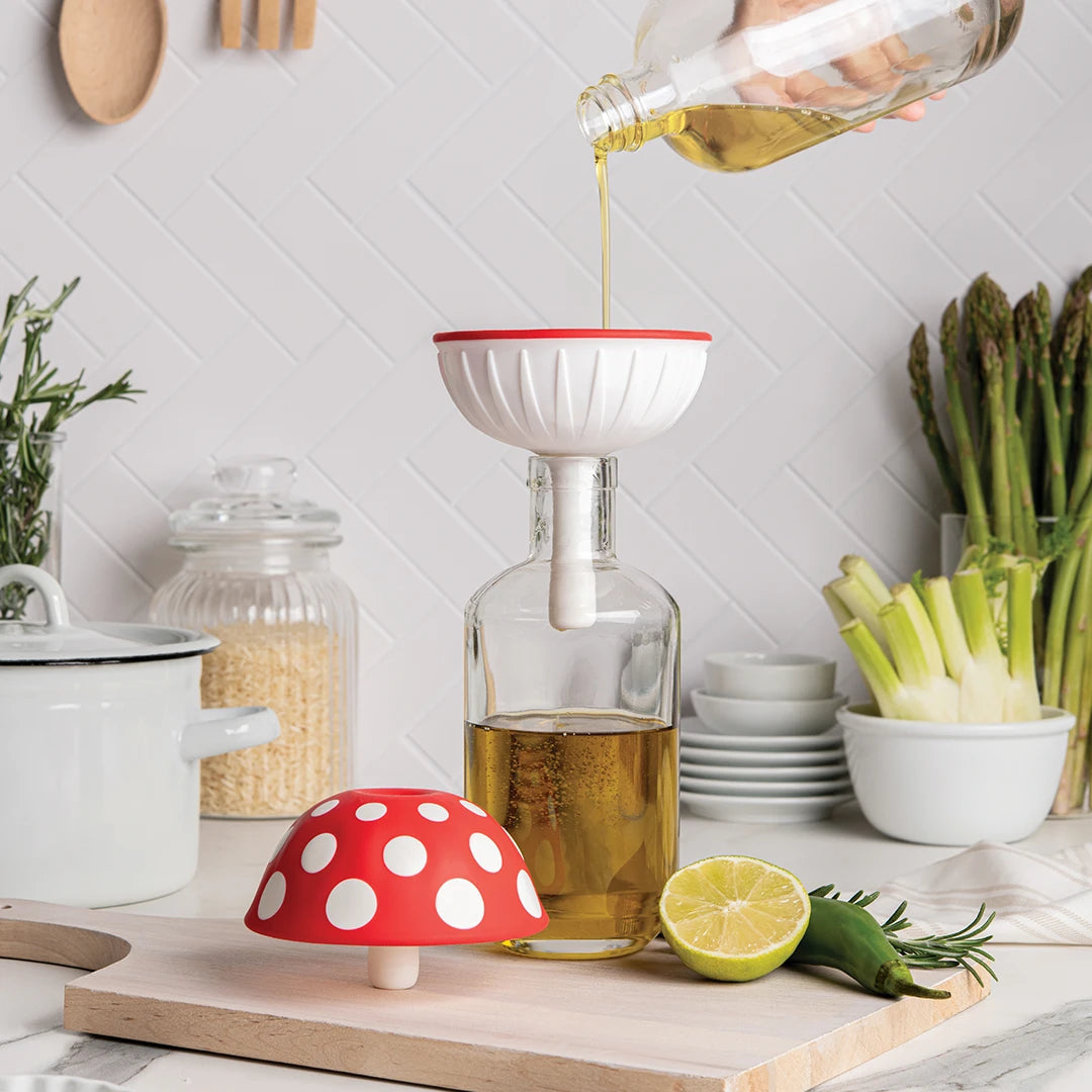 Pouring oil into a bottle using a mushroom-shaped funnel, with kitchen items in the background.