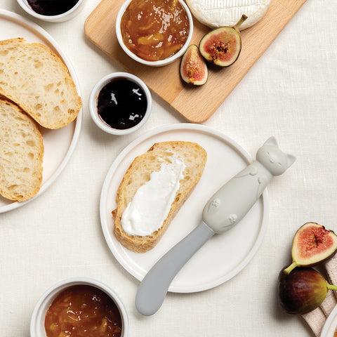 Bread, jam, figs, and a Mary Cat spreader sit on plates over a white tablecloth.