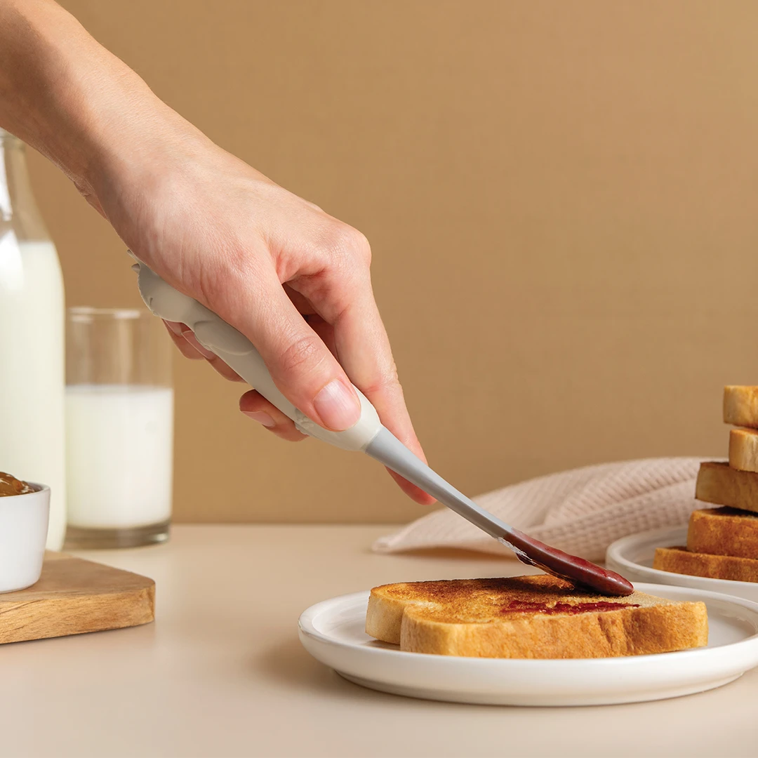 Spreading jam on toast with a knife; Mary Cat and milk in the background.
