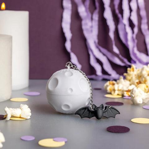 Moonlit: gray moon-shaped container with bat keychain, popcorn, candles, streamers & tea strainer.