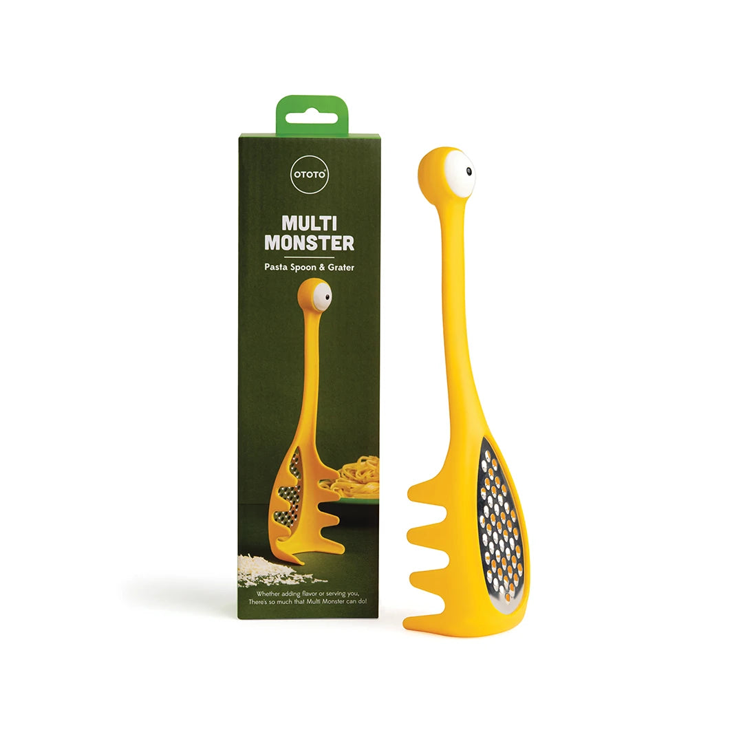 OTOTOs Multi Monster pasta spoon with cheese grater, yellow & styled like a cartoon monster, beside package.