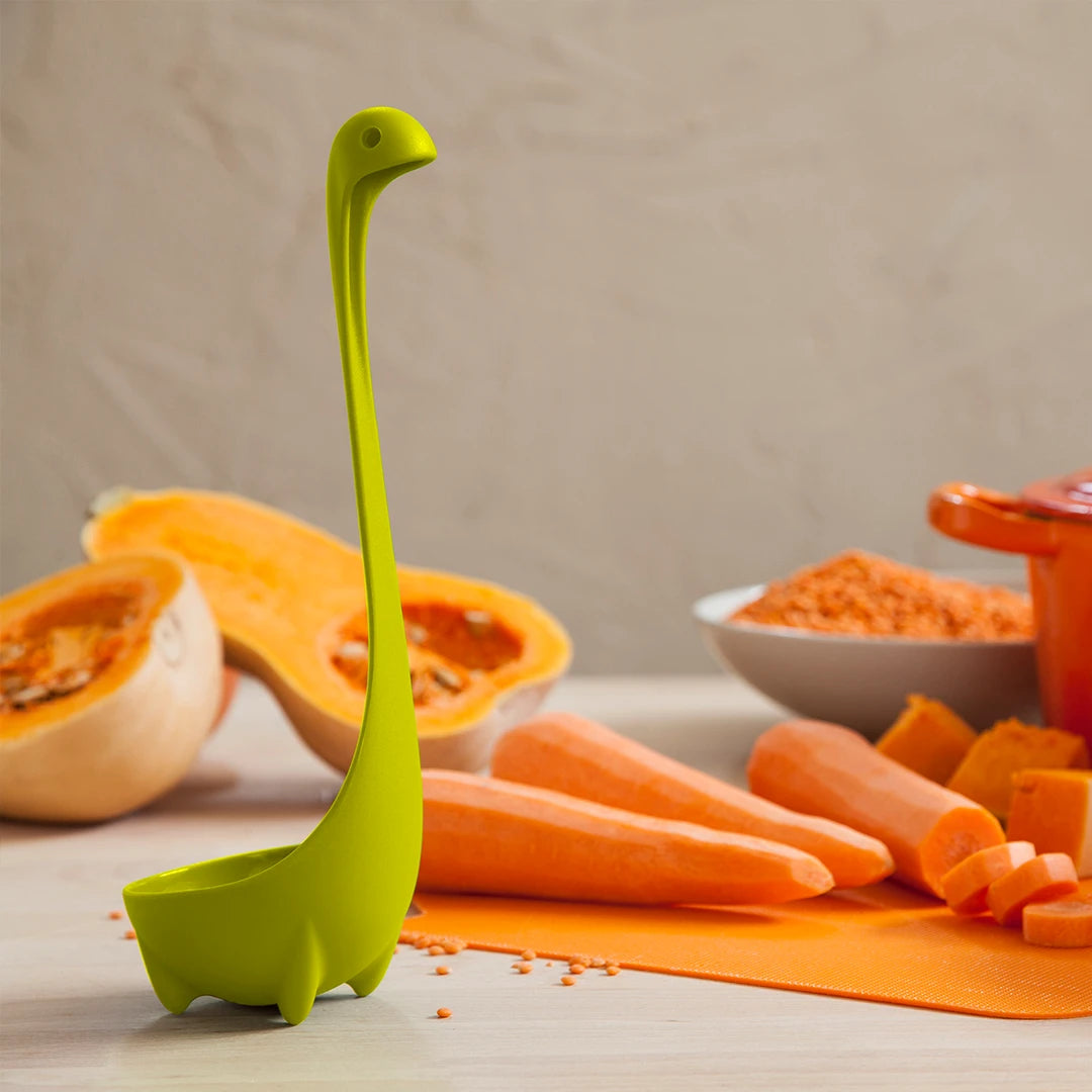 The Nessie ladle stands near chopped butternut squash and carrots on a kitchen counter.
