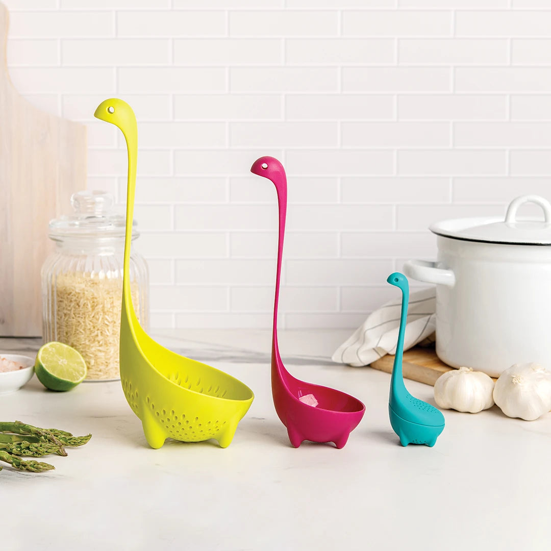 Nessie Family gadgets: colorful dino ladles rest on the counter with food in the background.