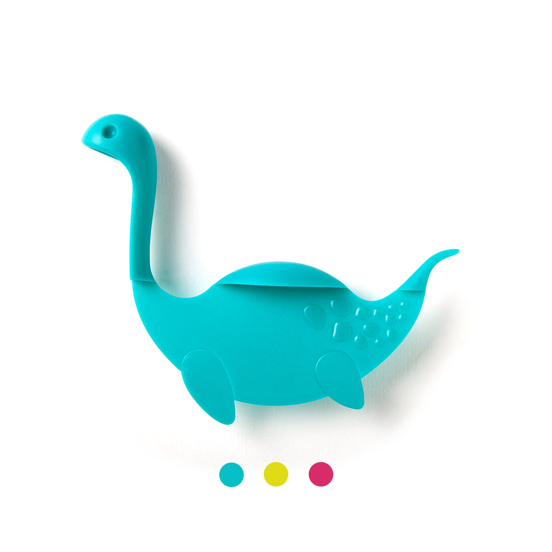 Blue dinosaur-shaped silicone utensil, resembling Nessie Tale, above a trio of colored dots.