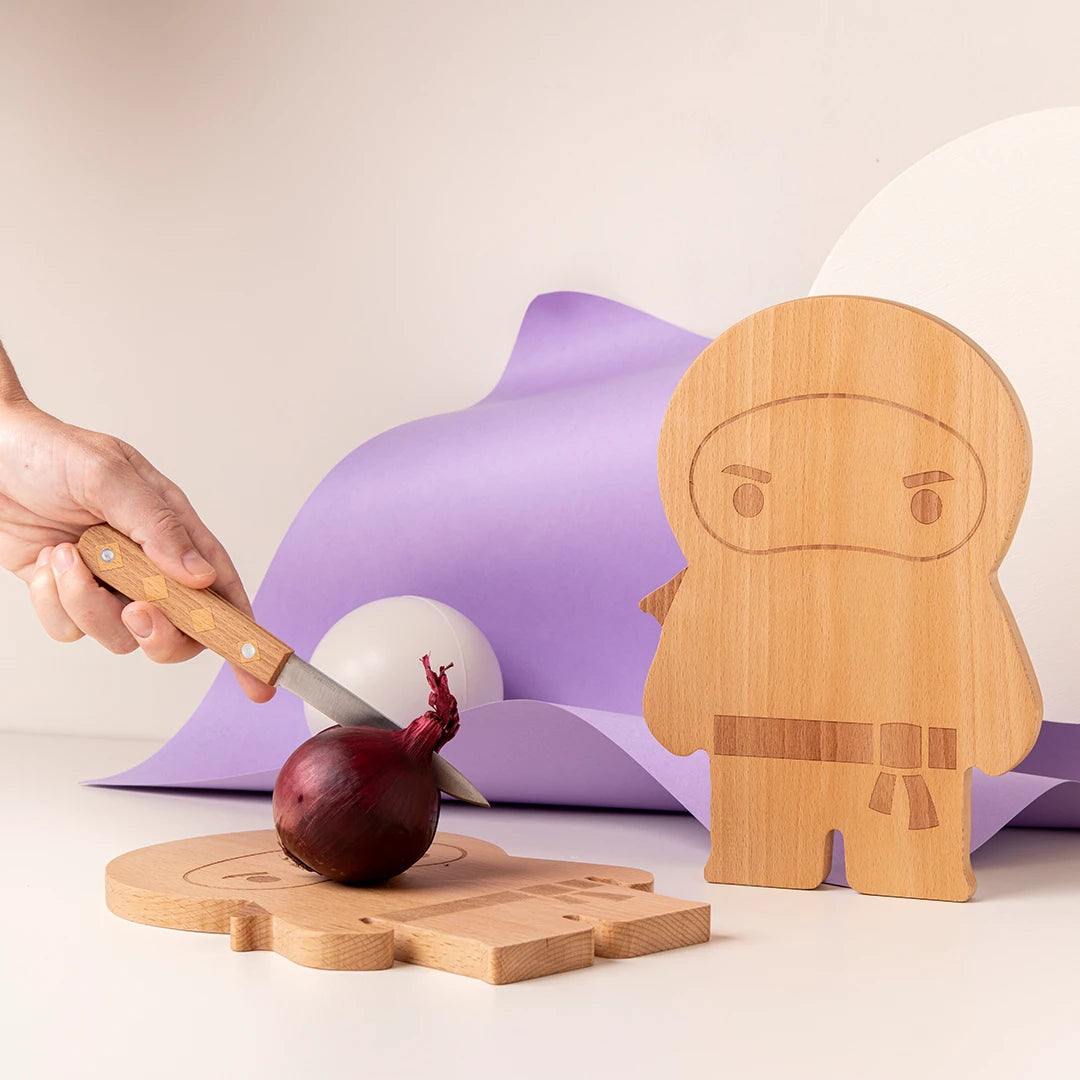 Hand slicing red onion on ninja-shaped wooden board, with purple background.