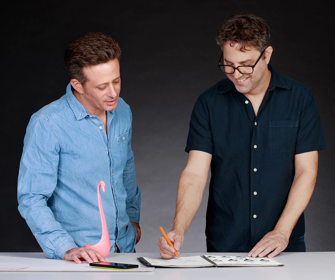 Two men discussing and drawing at a table with a pink flamingo ornament.