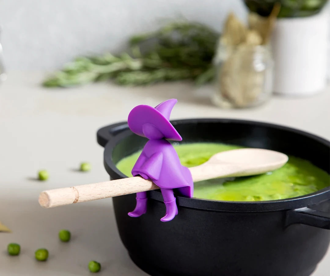 Purple wizard figure holds wooden spoon over pot of green soup.