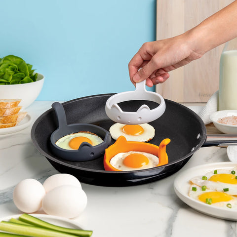 Hand using PanCats egg rings in skillet with sunny-side-up eggs by OTOTO.