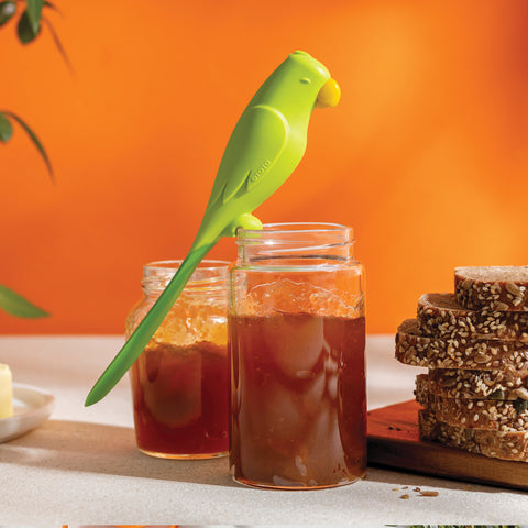 An OTOTO Parry green bird-shaped silicone spatula rests on a jam jar beside bread and another jar.